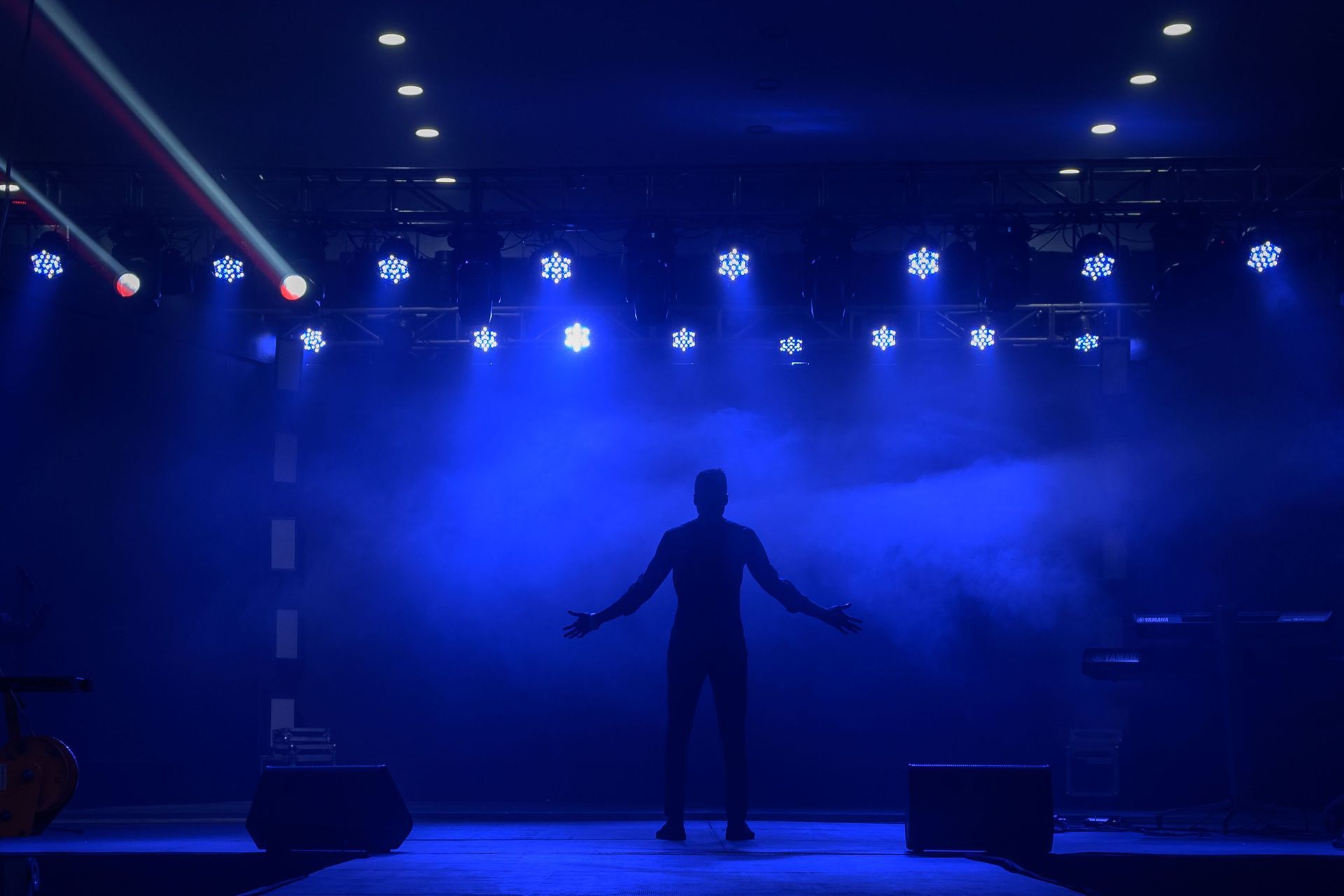 Silhouetted performer on a blue-lit stage with bright spotlights and fog