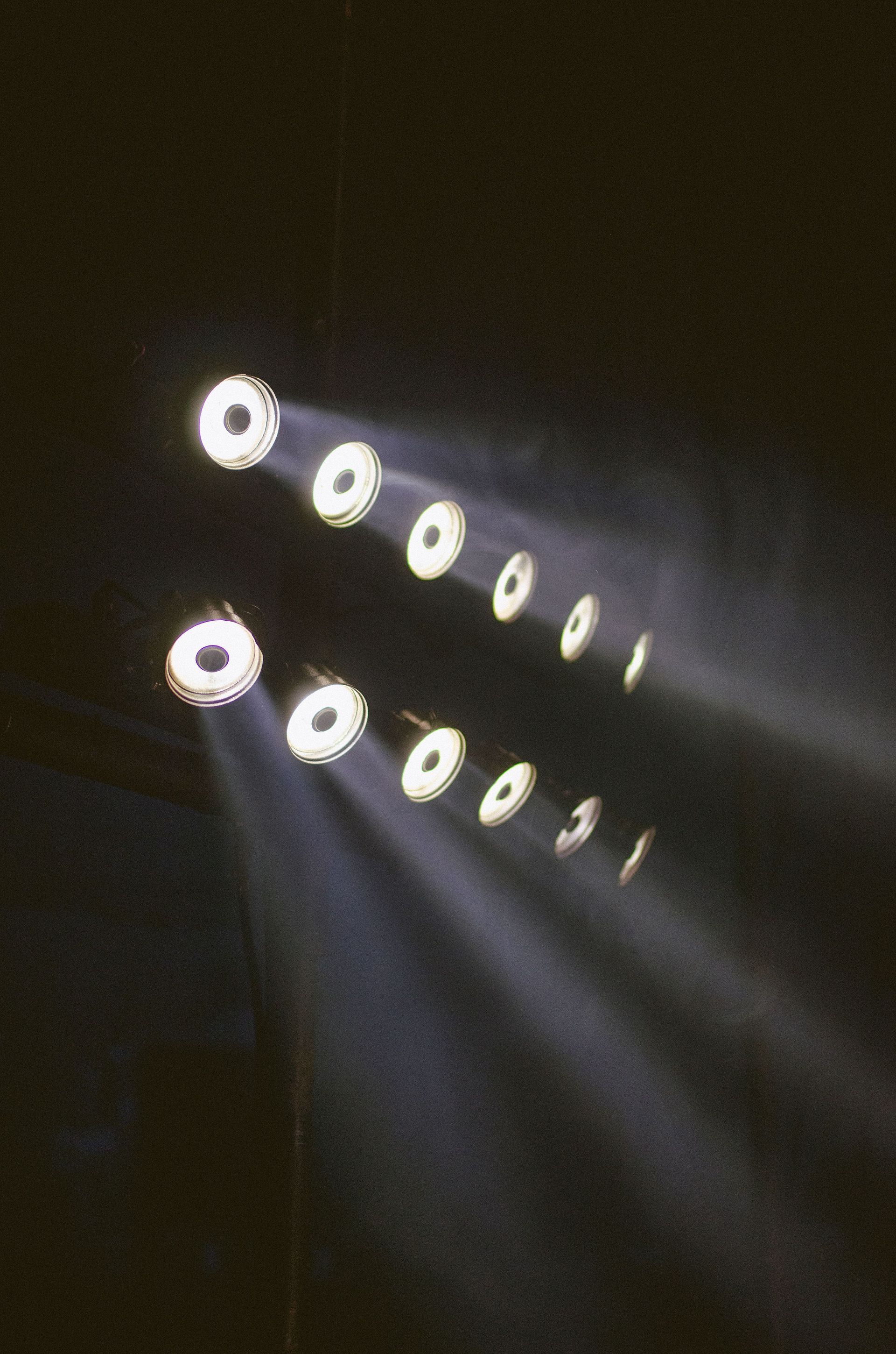Rows of bright circular lights casting diagonal beams in a dark room