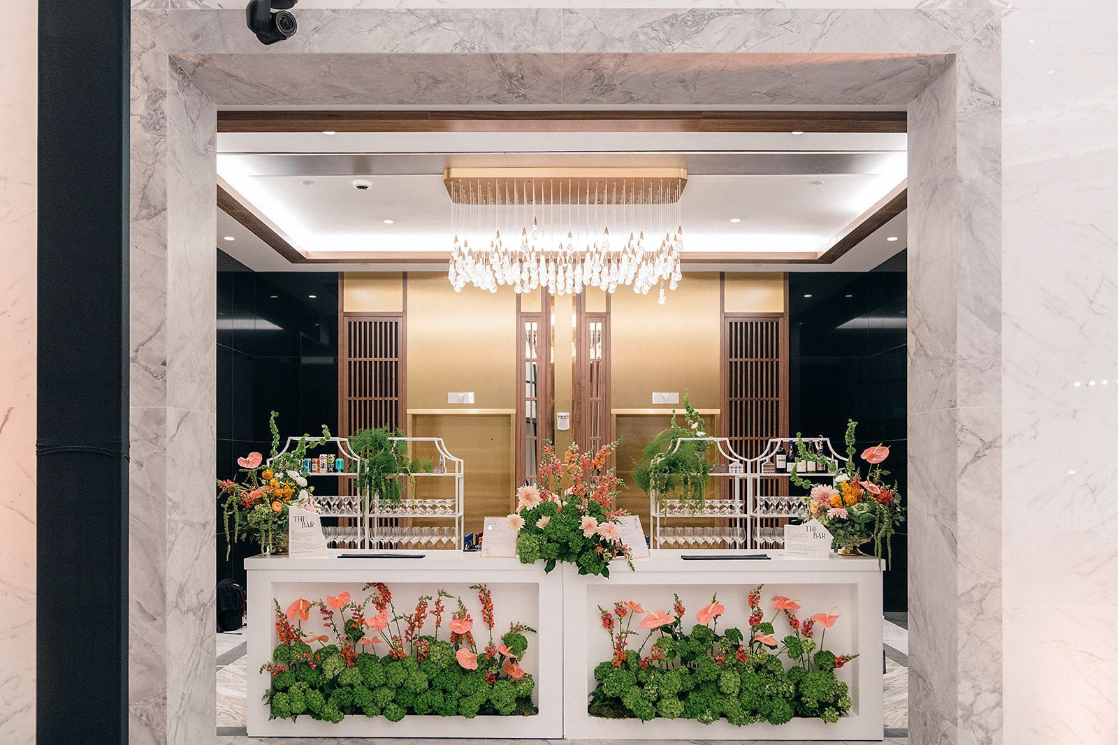 Elegant hotel lobby with marble entrance, floral displays, and chandelier.