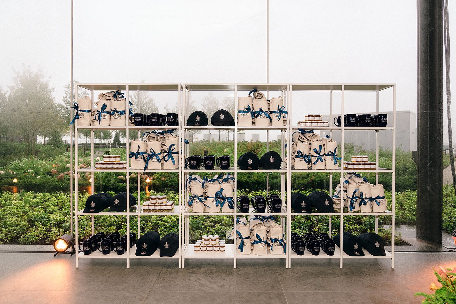 White shelving unit with gifts and caps, outdoors. Gifts wrapped in cream paper with blue ribbons.