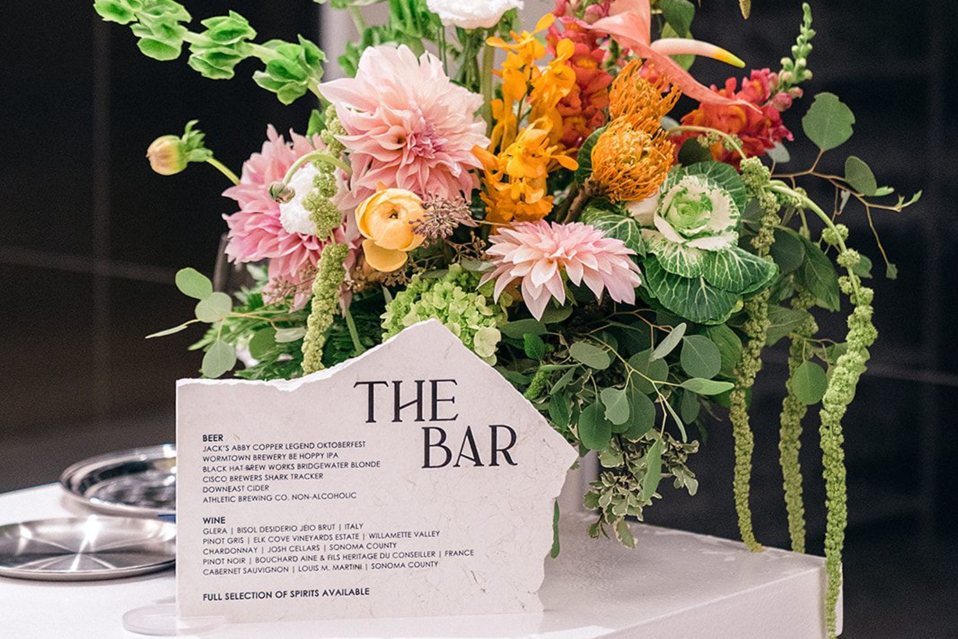Floral arrangement with bar menu; pink, orange, and green flowers with a white sign that reads
