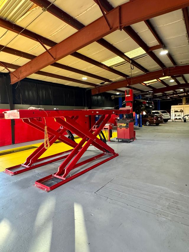 Red hydraulic car lift in a garage with high ceiling and overhead lights | Coastal Autoxpress