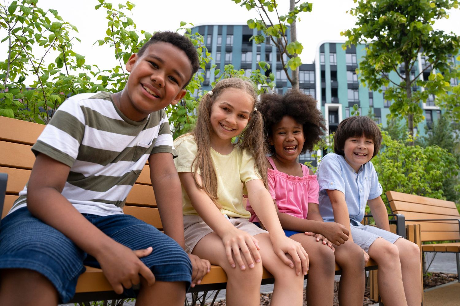 A group of children are sitting on a wooden bench in a park.