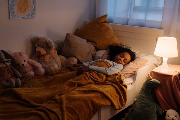 A little girl is sleeping in a bed with stuffed animals.