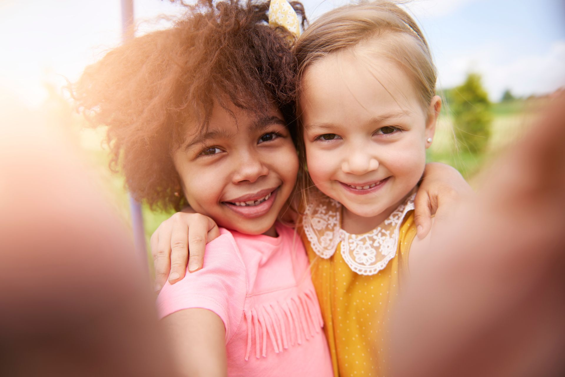 Two little girls are hugging each other and taking a selfie.