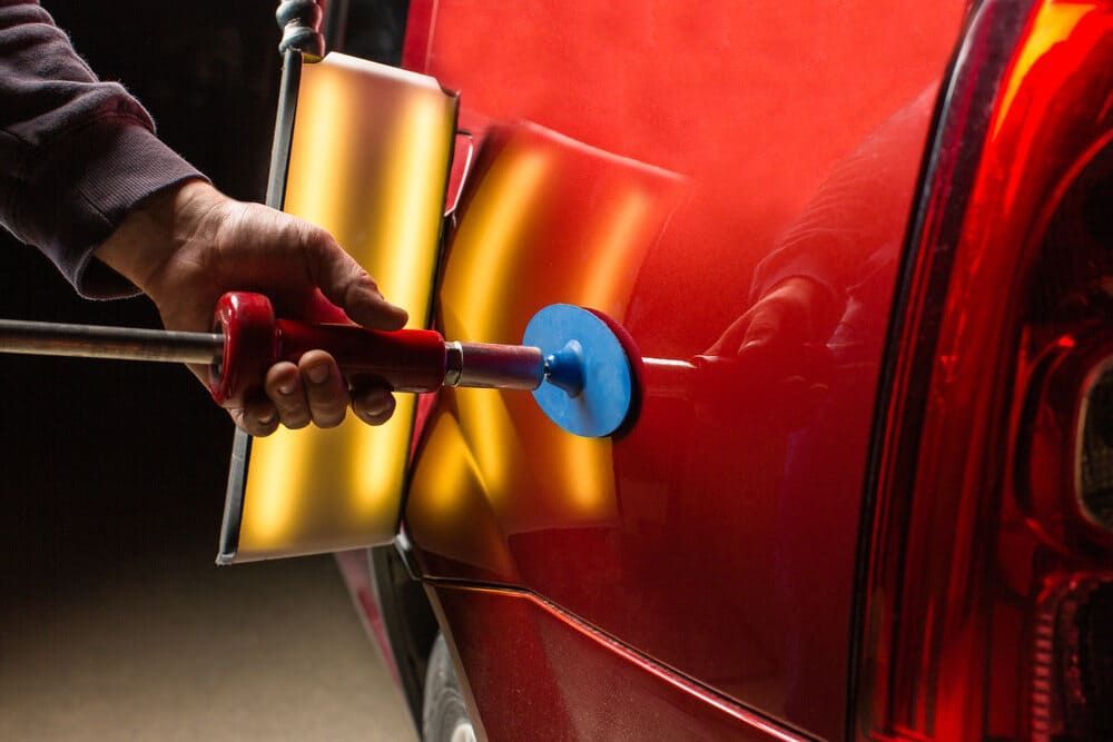 A Person Is Using A Tool To Fix A Dent On A Red Car — Mahers Smash Repairs in Nemingha, NSW