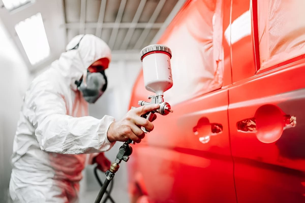 A Man In A Protective Suit Is Spray Painting A Red Van — Mahers Smash Repairs in Nemingha, NSW