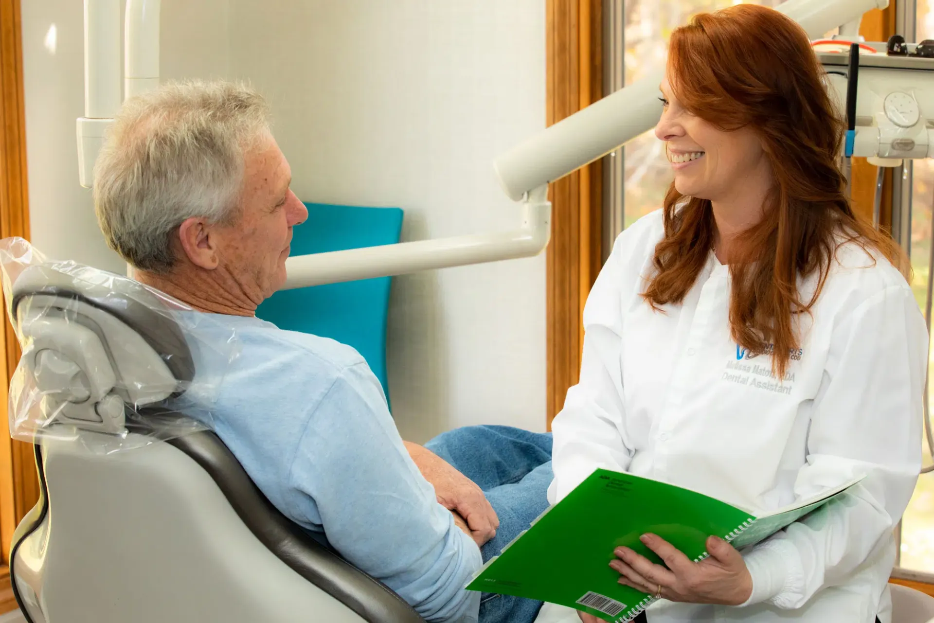 Dental patient consulting with a dentist in a clinic, holding a green clipboard.