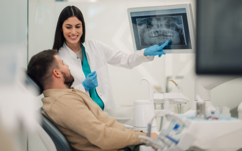 Dentist showing a patient an X-ray in a clinic, with dental tools on a tray