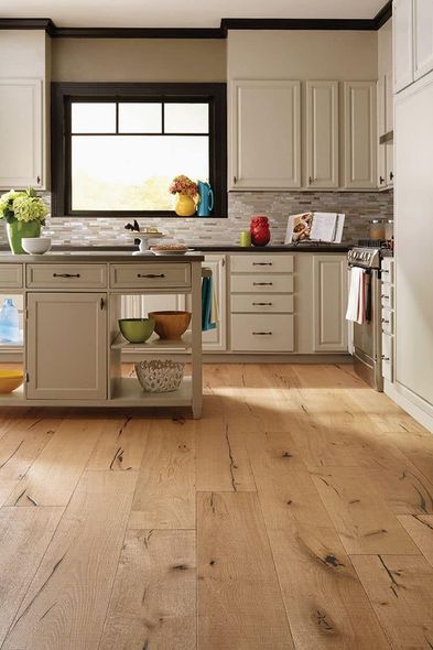 Kitchen with light wood floor, cream cabinets, island, and window with colorful accents.