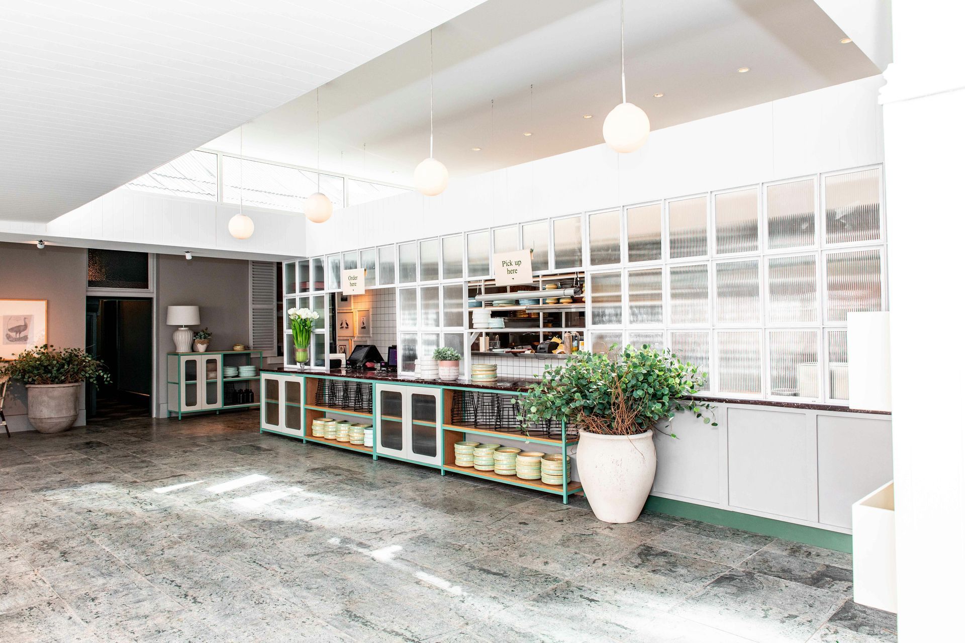 Bright, airy cafe interior with a counter, pastries, plants, and a large window.