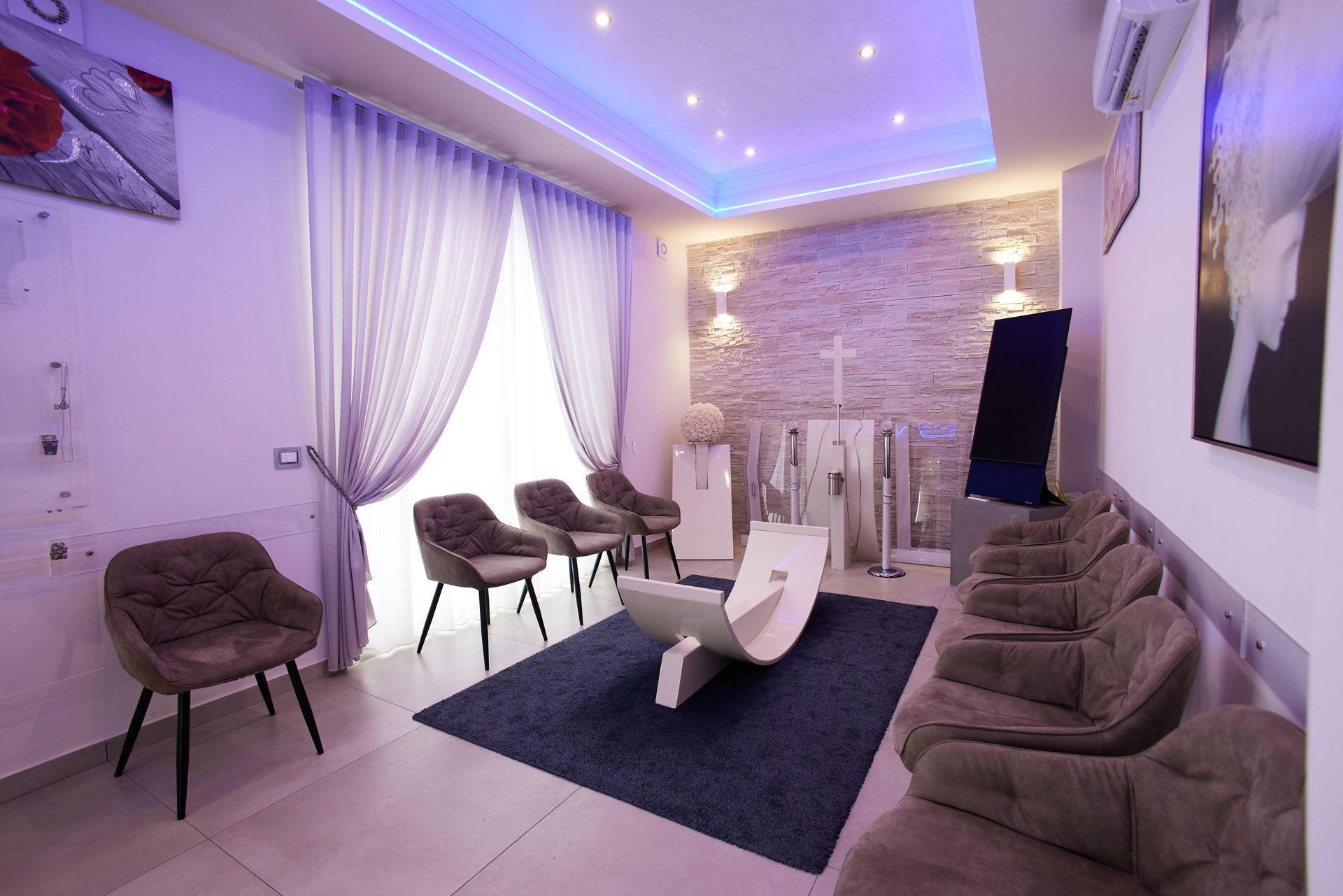 Una sala d'attesa di uno studio dentistico con illuminazione viola, diverse sedie e un design moderno.