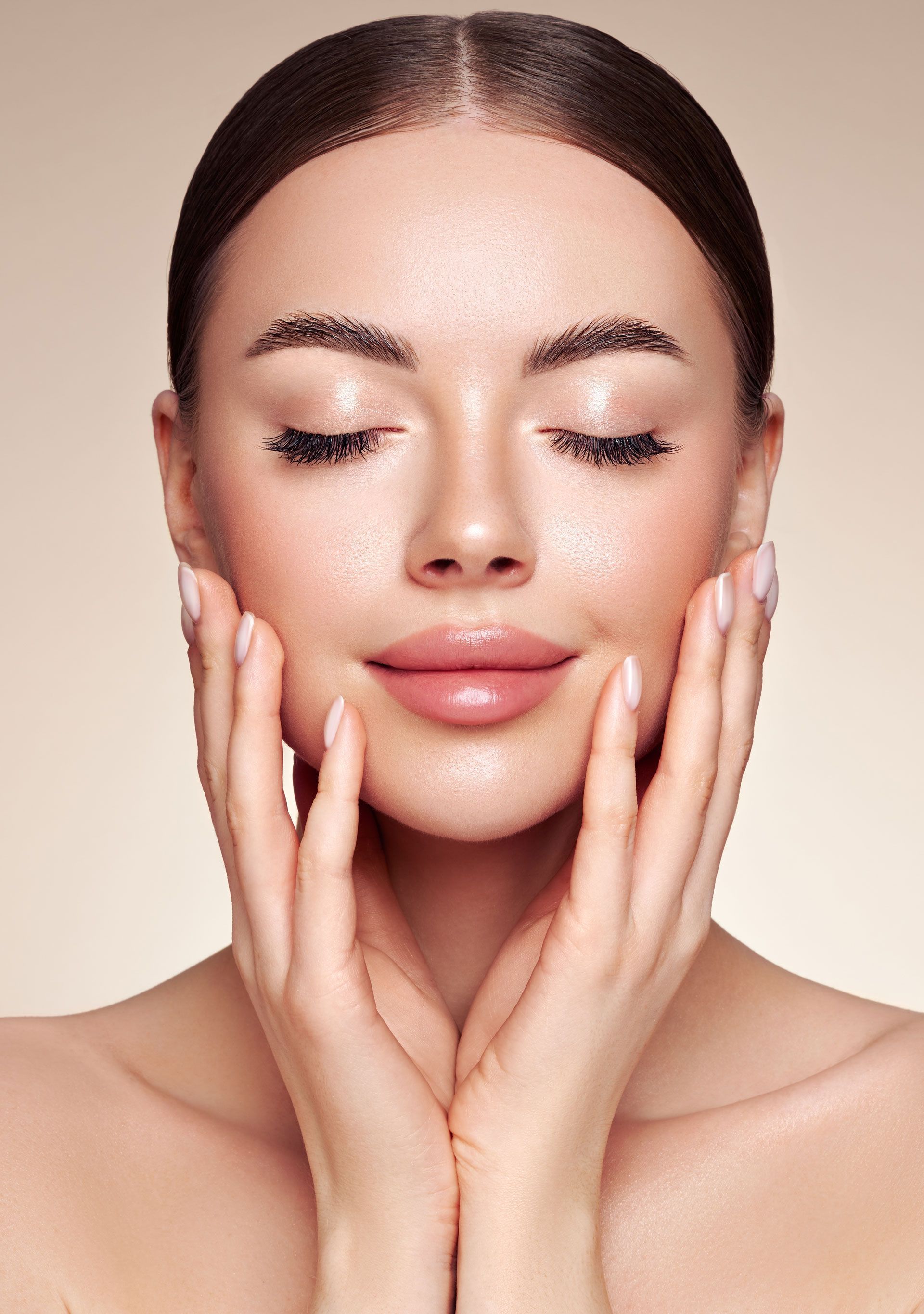 Close-up of a woman with eyes closed, gently touching her cheeks, against a soft neutral background.