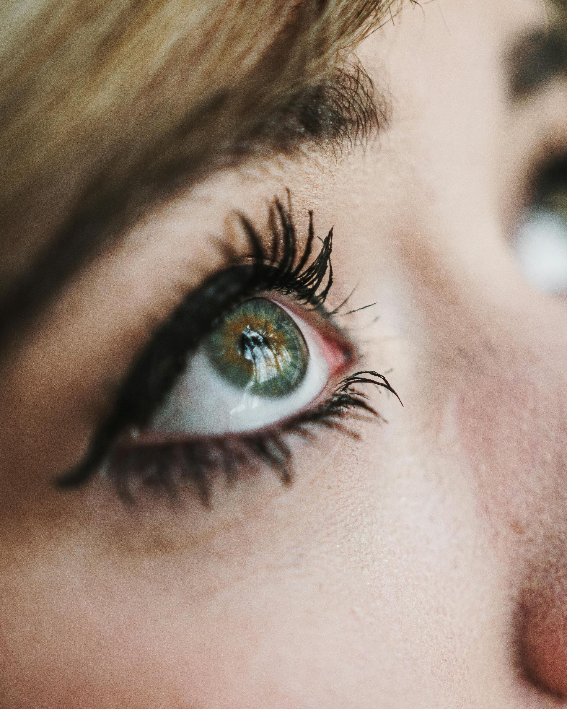 Close-up of a green eye with dark mascara and a blurred reflection of a face in the pupil