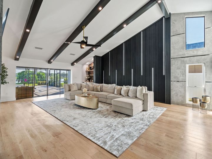 Modern living room with beige sectional, black curtains, light wood floors, and large windows