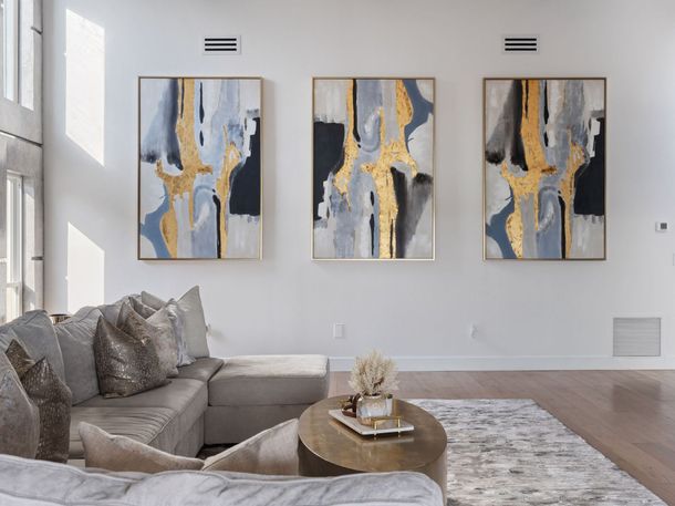Modern living room with gray sofa, round coffee table, rug, and three abstract paintings on a white wall