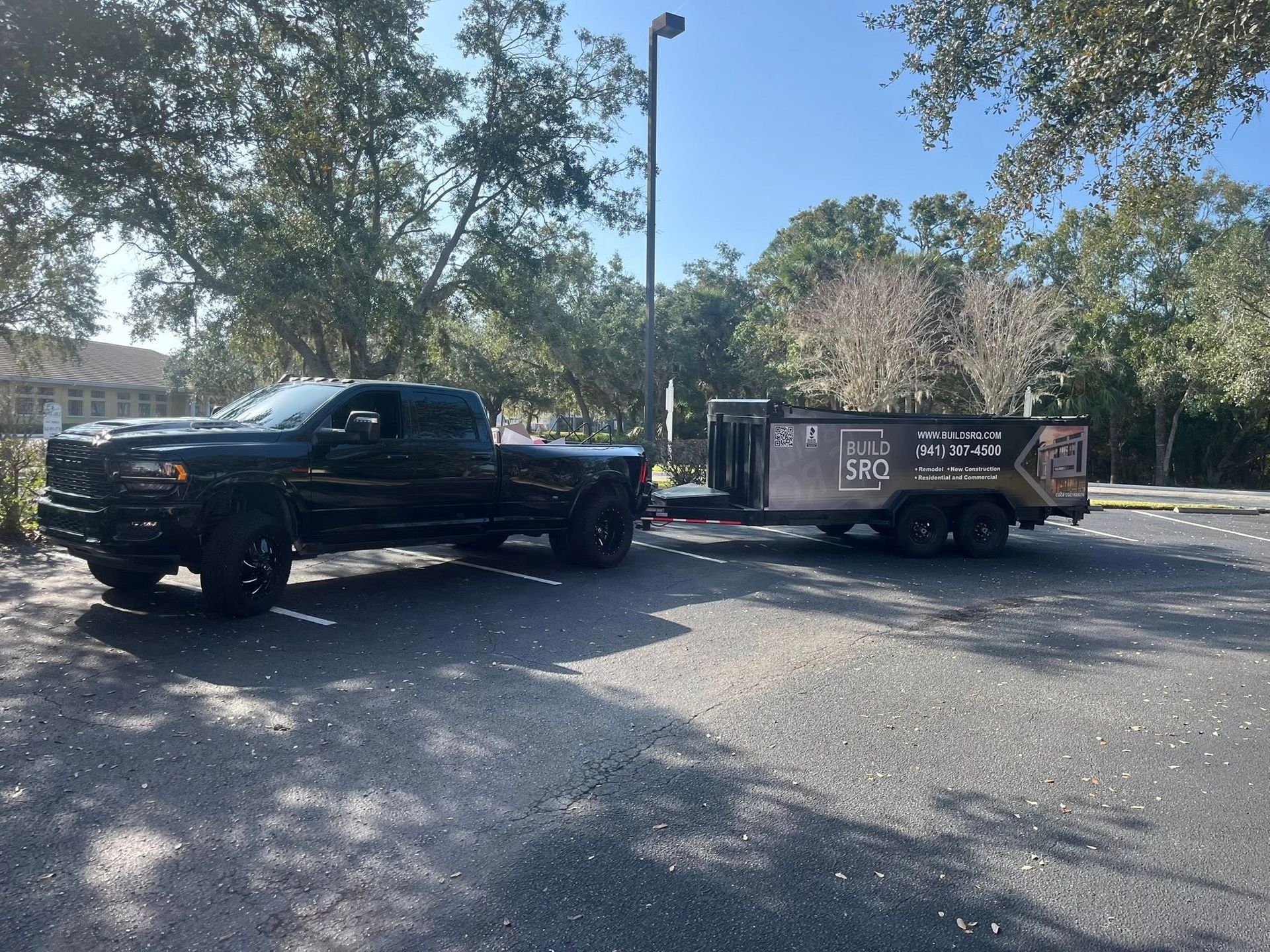 Black pickup truck towing a utility trailer in a sunny parking lot under trees