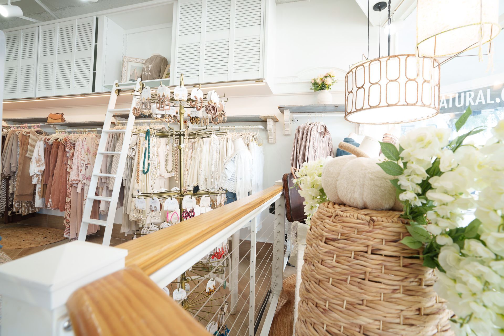 Bright boutique interior with white shelves, hanging garments, and a woven pumpkin display with flowers