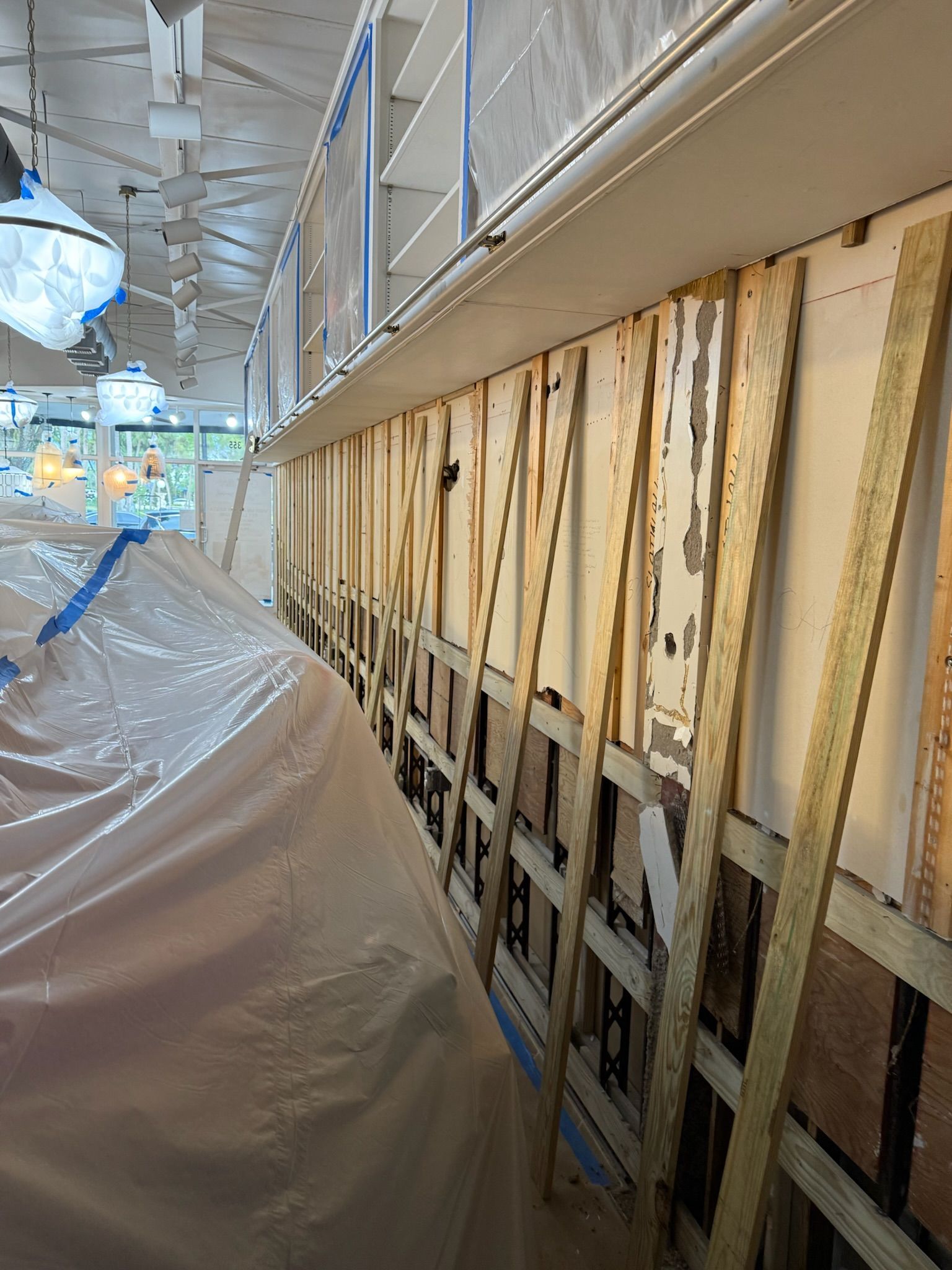 Construction site with exposed wall framing beside a tarp-covered walkway under a metal ceiling