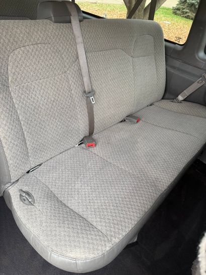 Gray patterned car bench seat with a seat belt hanging across it.