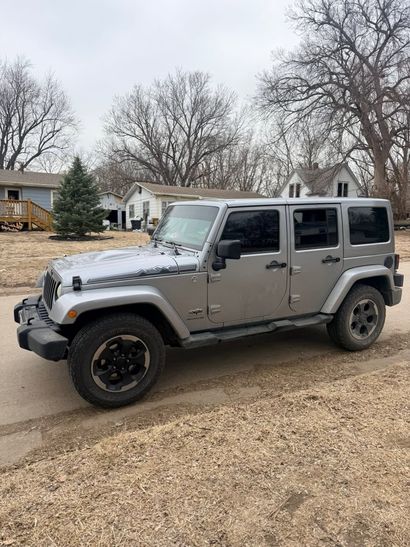 Gray four-door Jeep Wrangler parked on a residential street on an overcast day