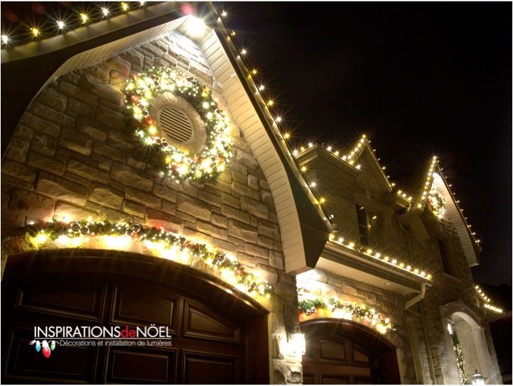 Des lumières de Noël décorent une maison en briques la nuit, notamment une couronne et des guirlandes lumineuses soulignant le toit et les portes du garage.