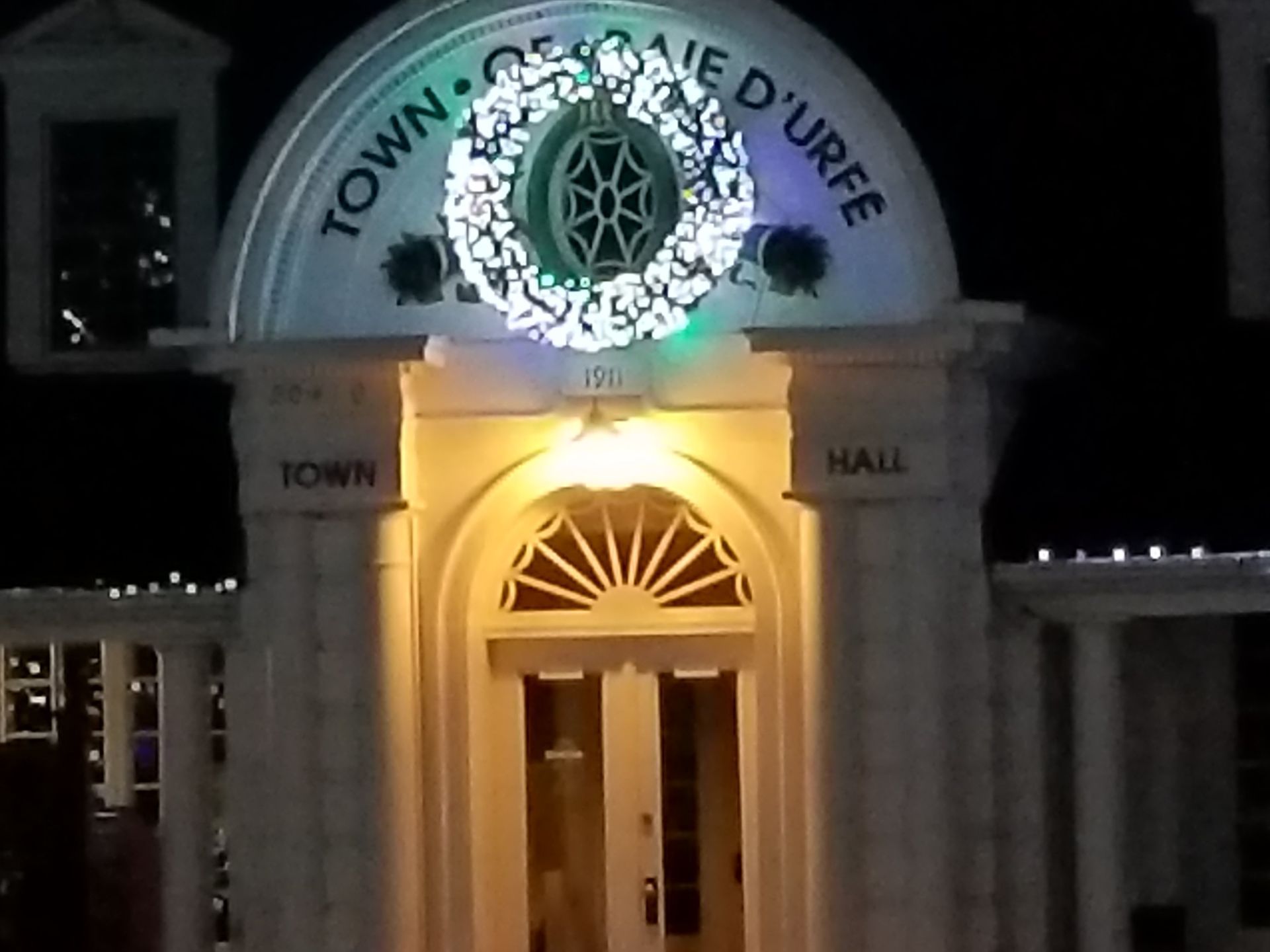 Hôtel de ville illuminé la nuit par une couronne de Noël. « VILLE DE BAIE D'URFE » est inscrit sur l'arche.