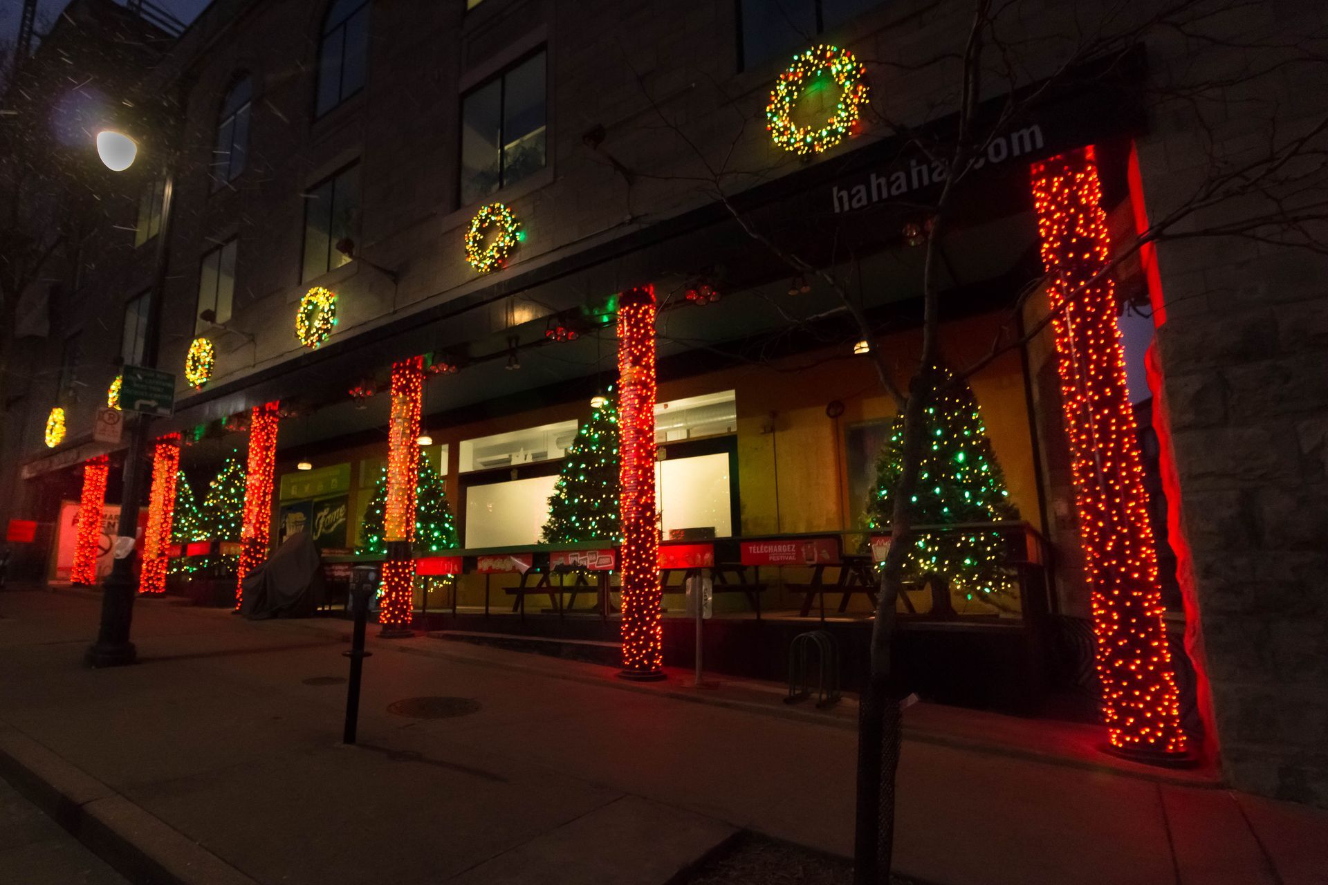Un bâtiment illuminé de lumières de Noël : colonnes rouges, couronnes vertes et arbres décorés.