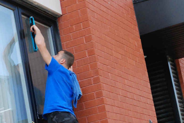 A man in a blue shirt is cleaning a window on a brick building.