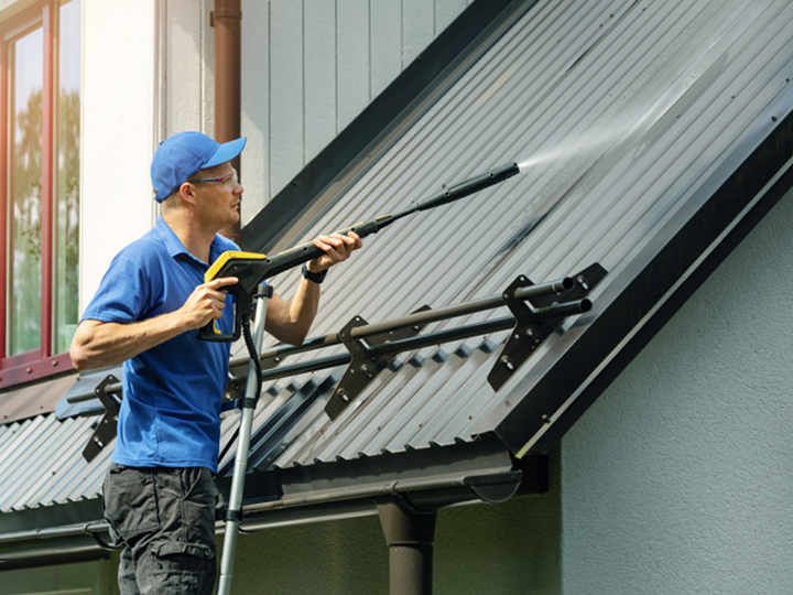 Un homme nettoie à haute pression le toit métallique d'une maison, à l'extérieur.