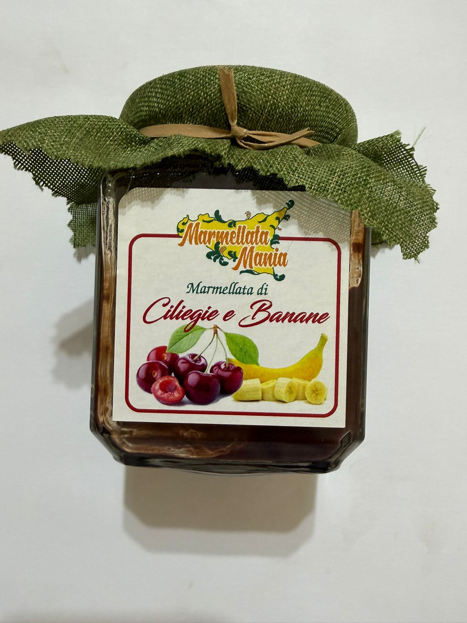 Vasetto di marmellata di mango con coperchio avvolto in una foglia verde ed etichetta con uva e banana.
