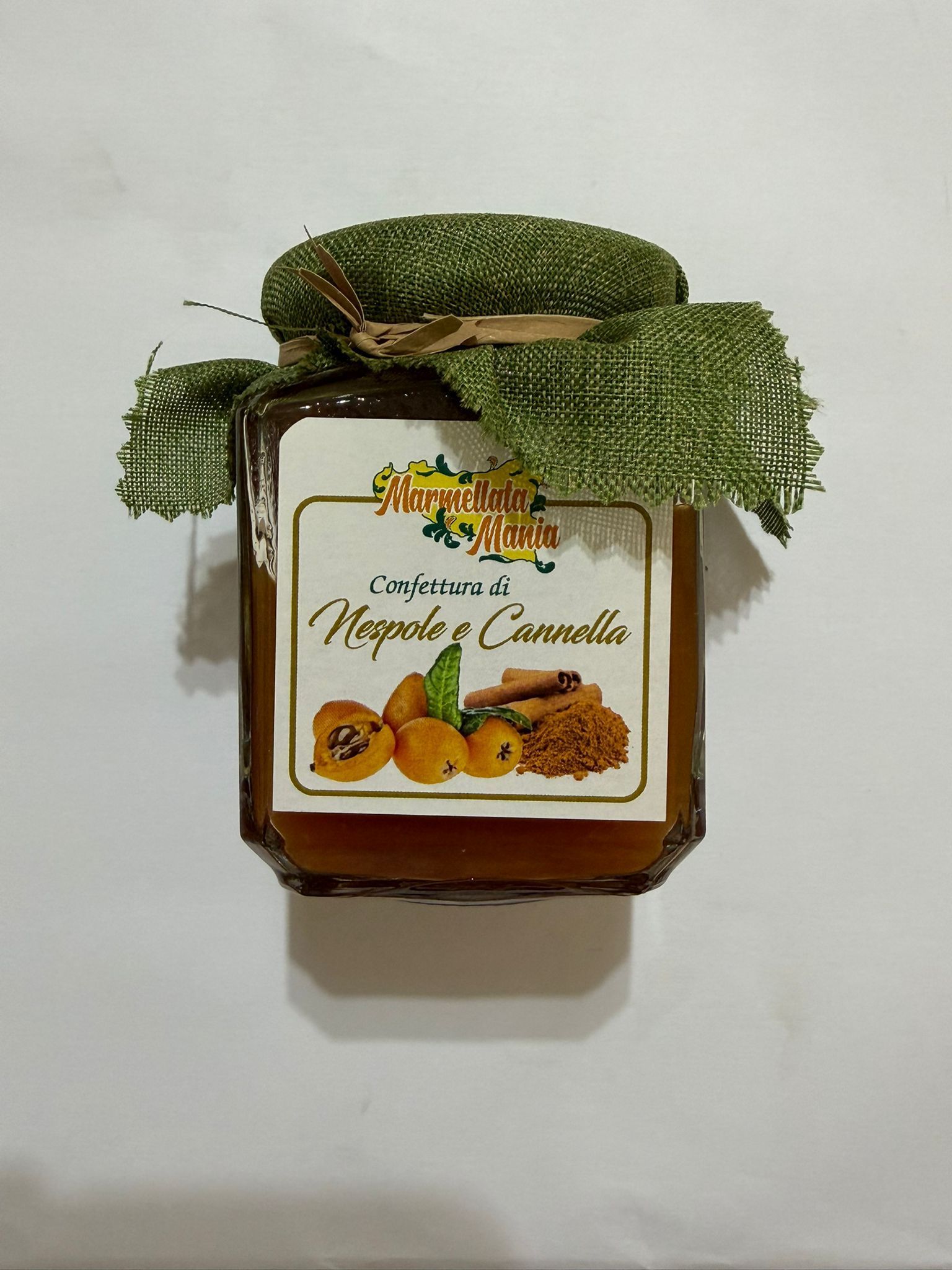 Vasetto di marmellata frizzante di mele e cannella con nastro decorativo verde e foglie essiccate su sfondo bianco.