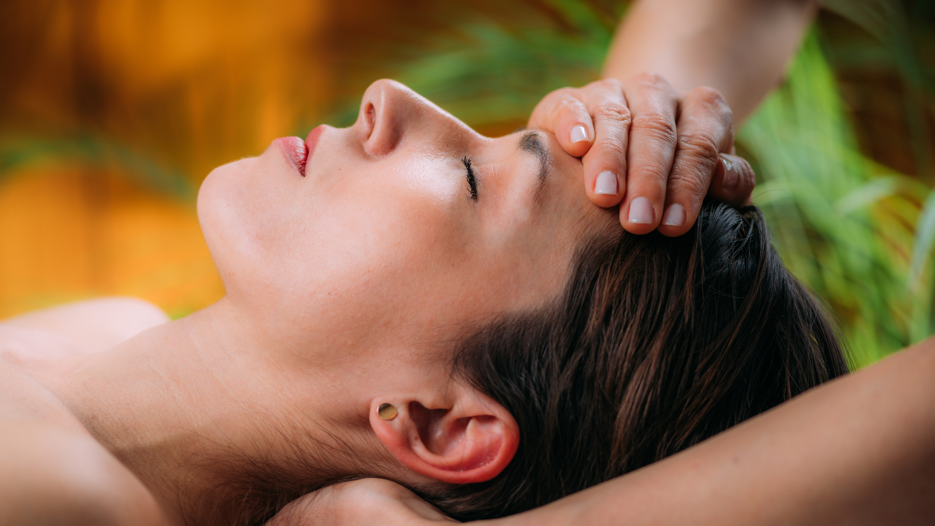 Person lying back with eyes closed while another hand massages their forehead, outdoors in warm light, craniosacral therapy
