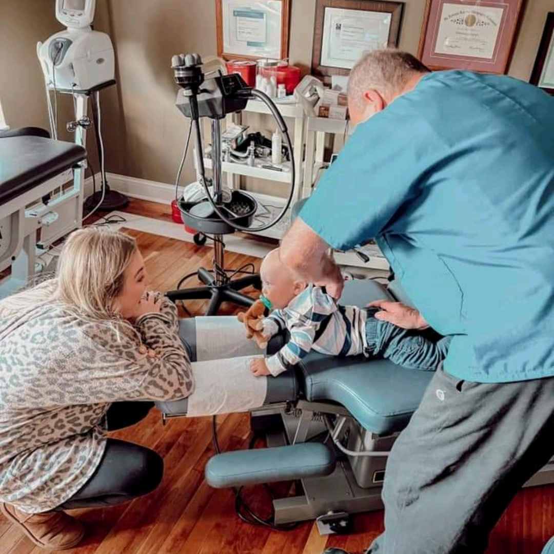 A man and a woman are kneeling down next to a child in a dental chair.