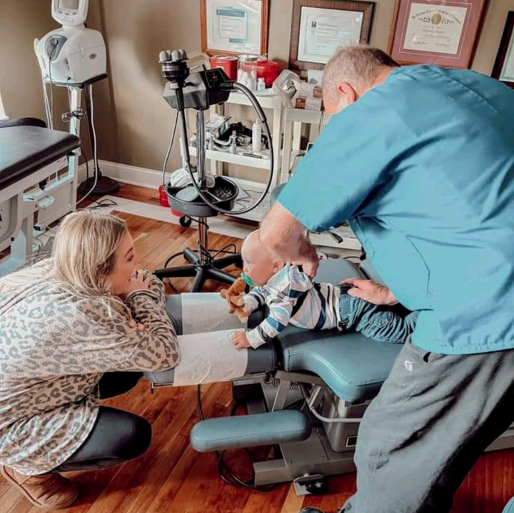 A man and a woman are kneeling down next to a child in a dental chair.