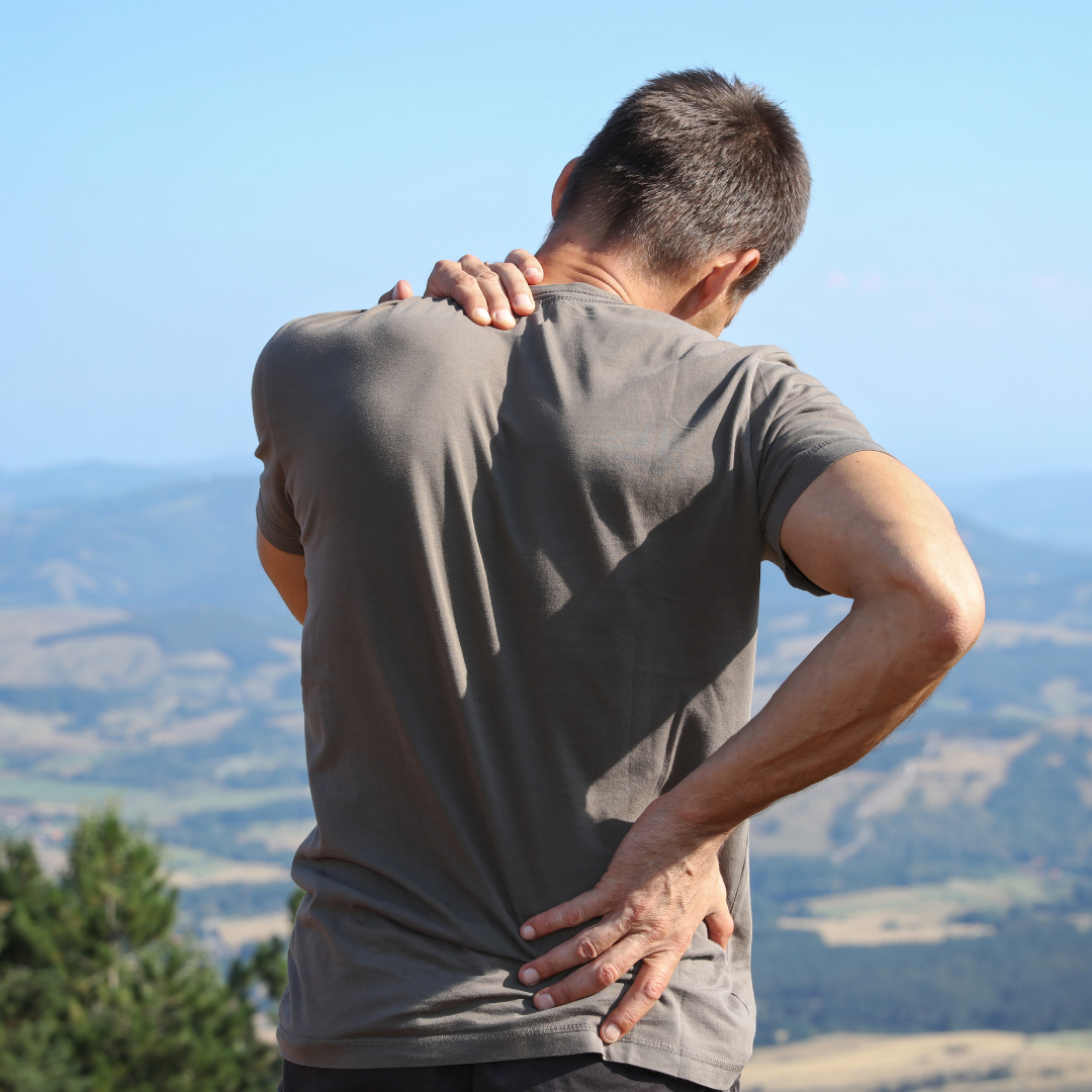 A man in a grey shirt is holding his back in pain