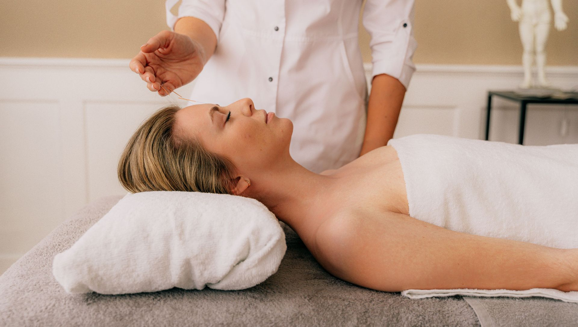 Facial spa treatment in a serene treatment room, with a client lying on a massage table and a therapist applying product.