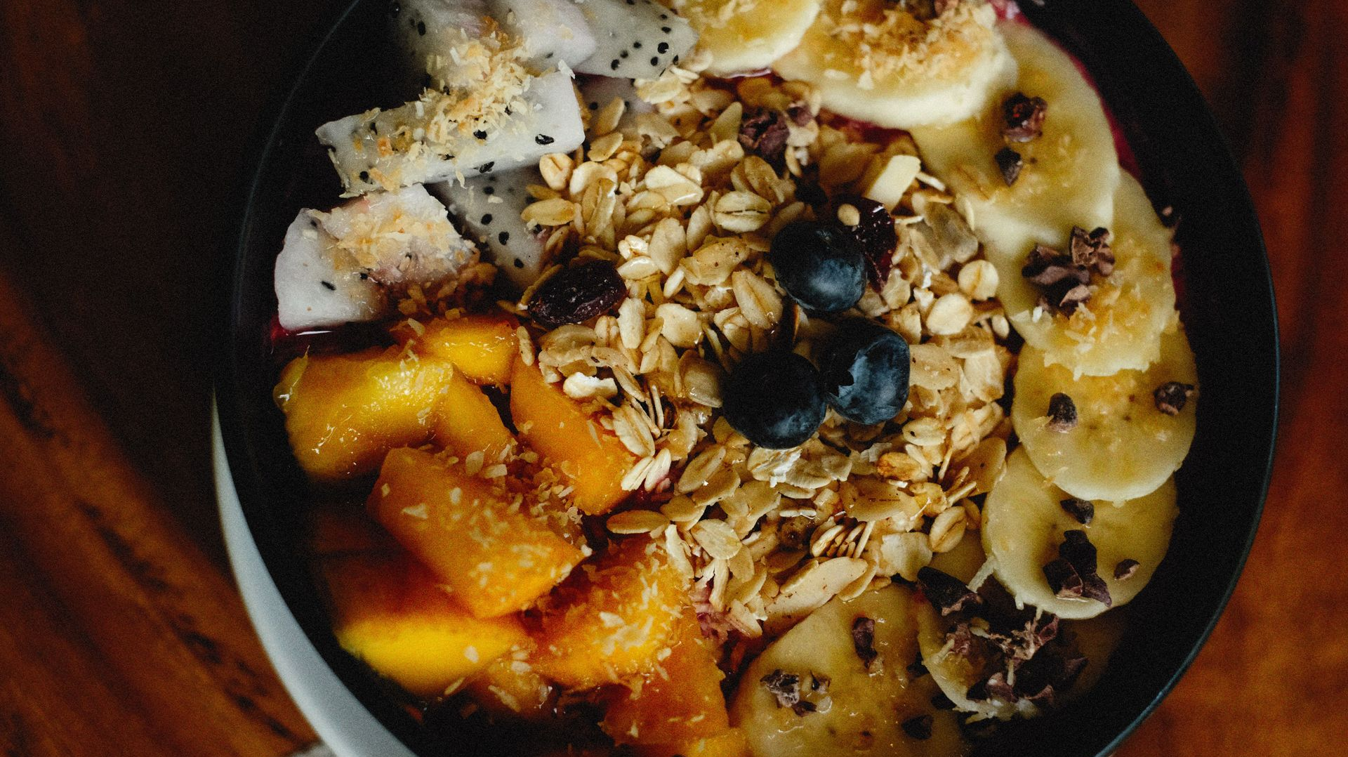 Bowl of oatmeal topped with bananas, berries, granola, and orange fruit pieces