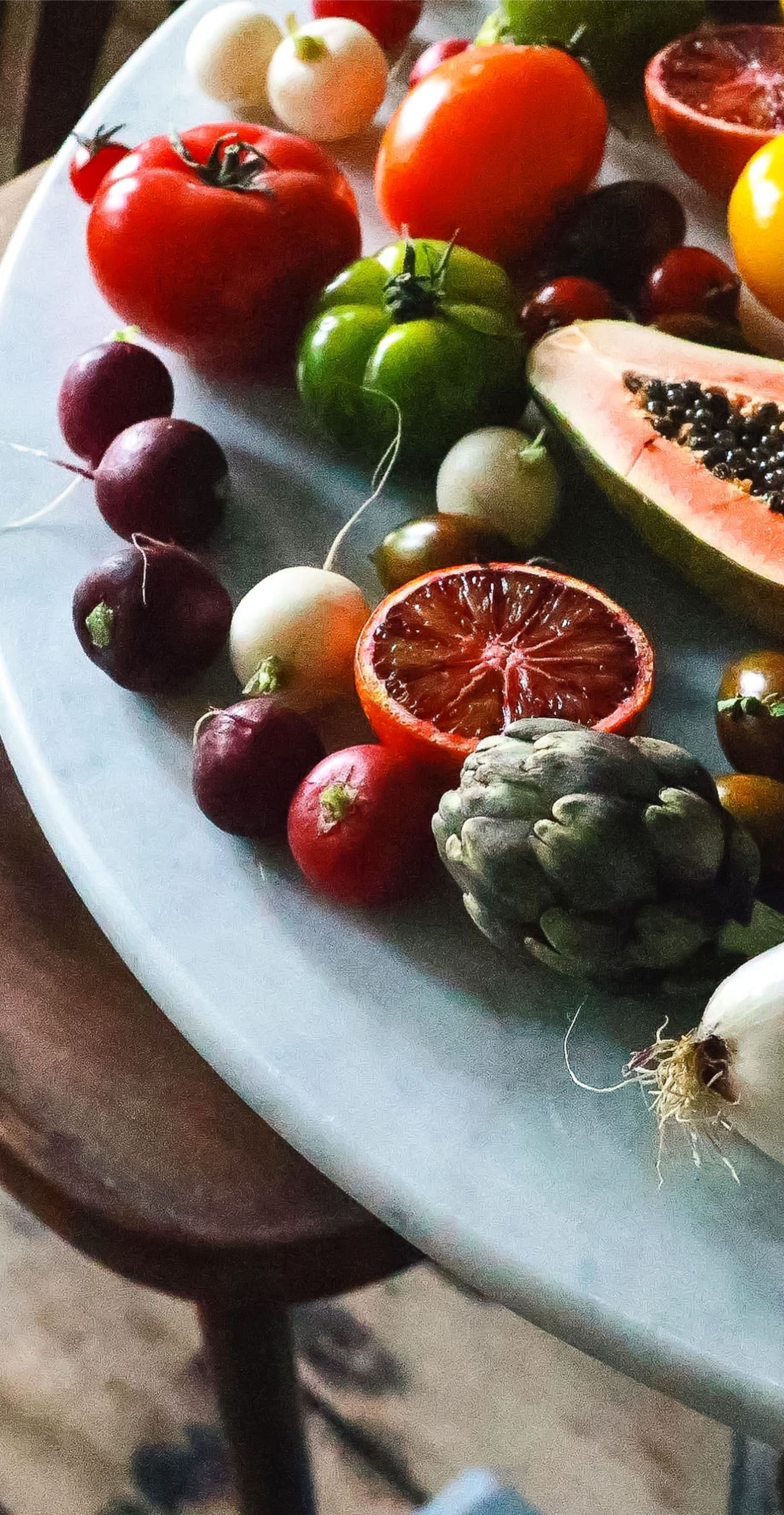Assorted colorful fruits arranged on a table, including tomatoes, citrus, grapes, and a halved papaya.