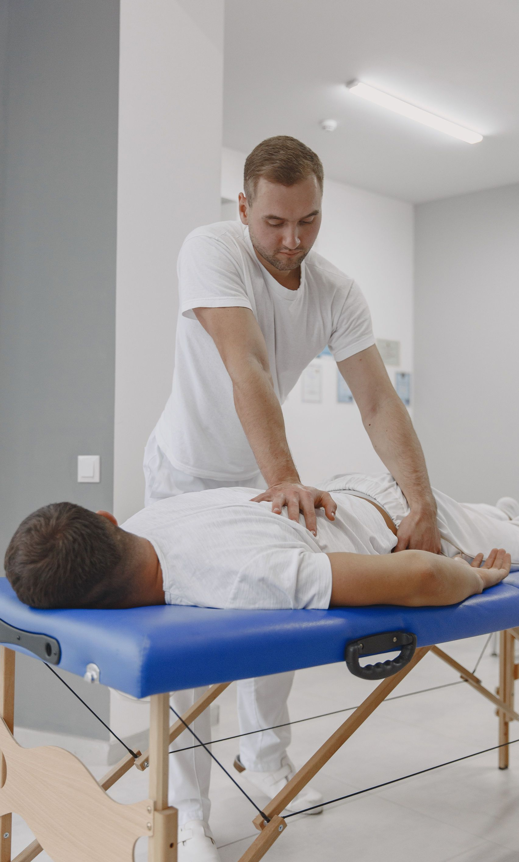 Massage therapist working on a person lying face down on a blue massage table in a bright room