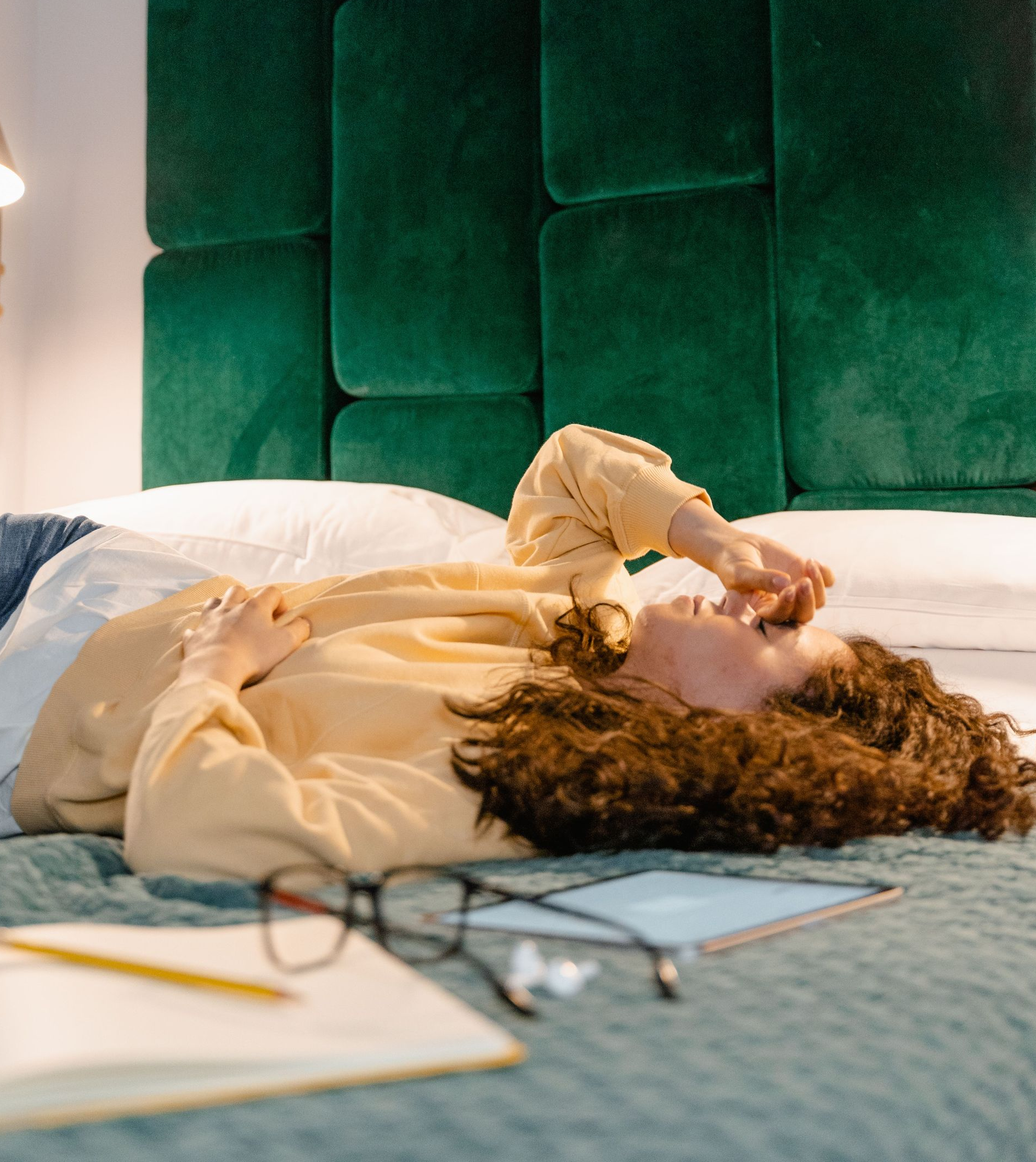 Person lying on a bed using a smartphone, with glasses and a notebook in the foreground.