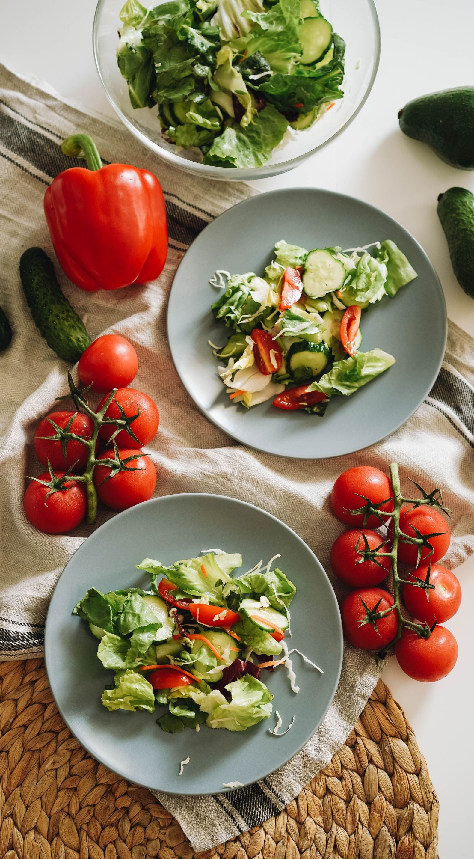 Three plates of fresh salad with tomatoes, peppers, and greens on a light tabletop