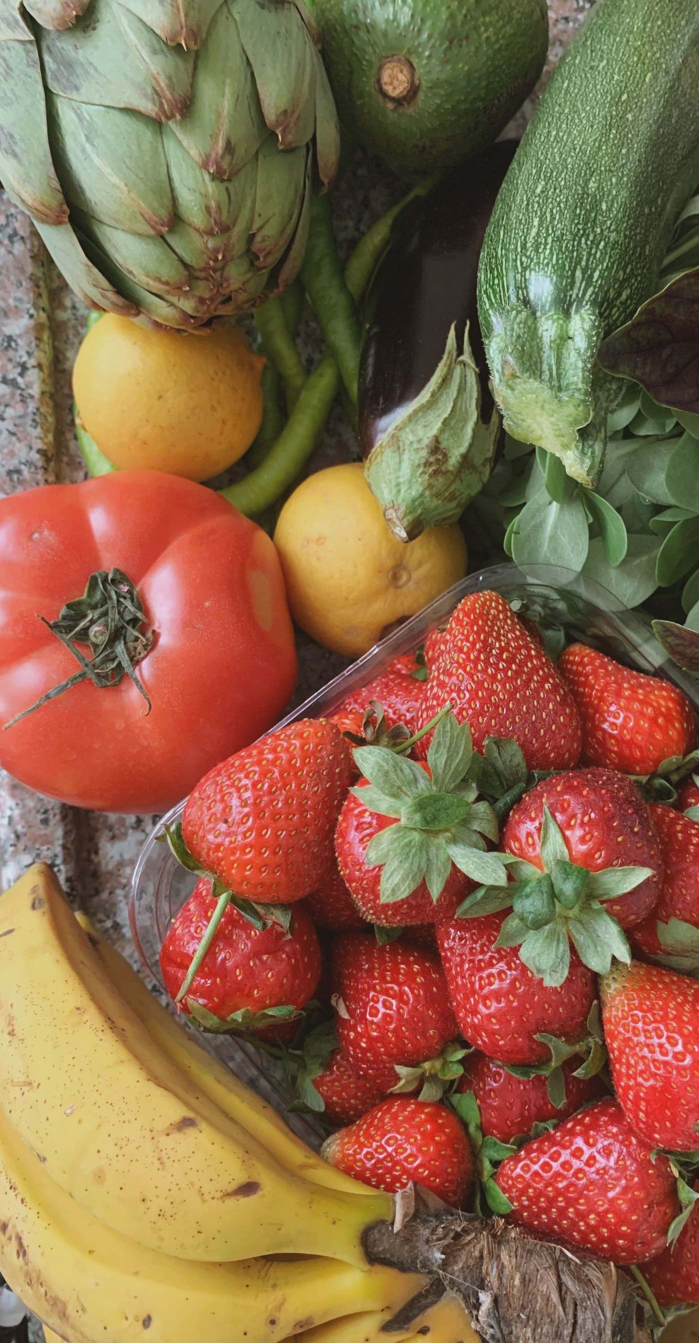 Assorted fresh fruits and vegetables, including strawberries, bananas, artichokes, and peppers, in a colorful display