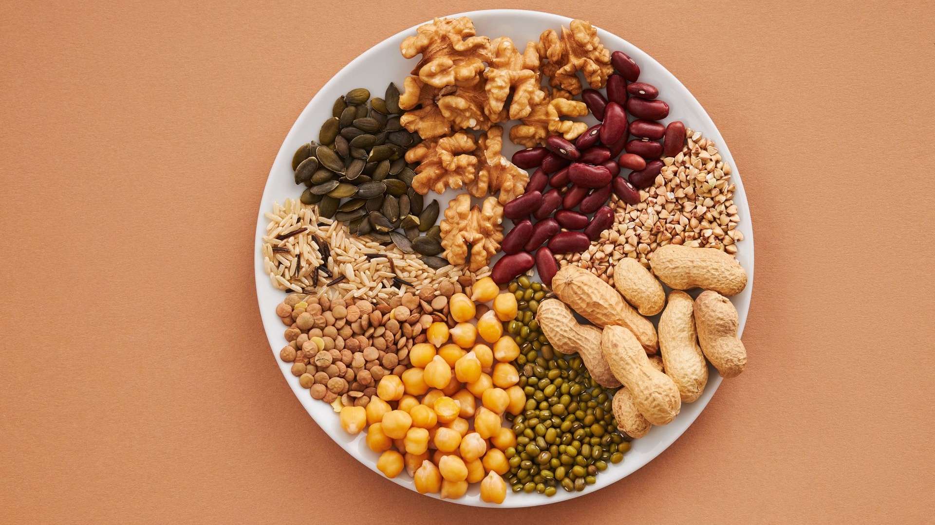 Top-down view of a plate with assorted nuts, beans, and seeds on a peach background