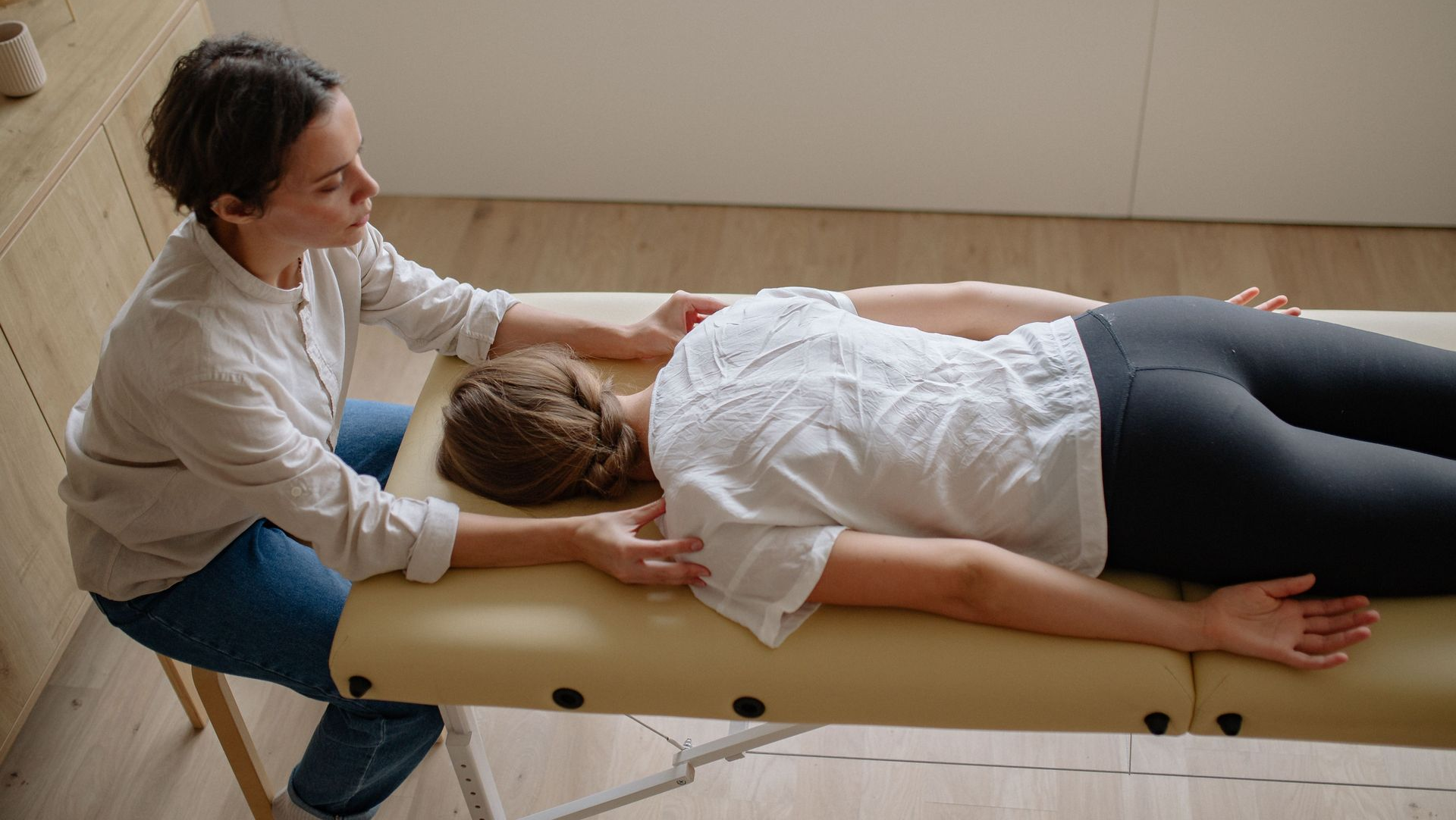 Therapist massaging a client lying face down on a treatment table in a bright room