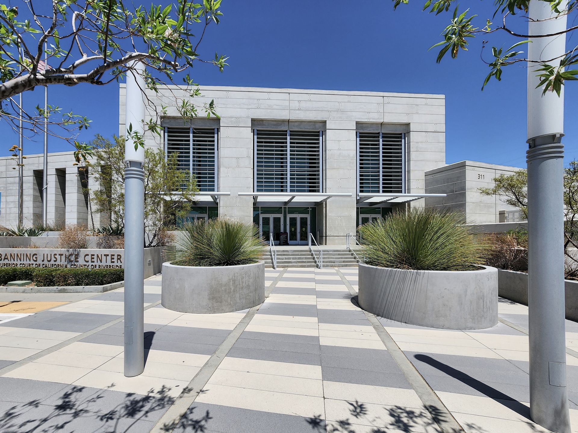 The modern, light-colored stone facade of the Banning Justice Center under a clear blue sky, with concrete planters.