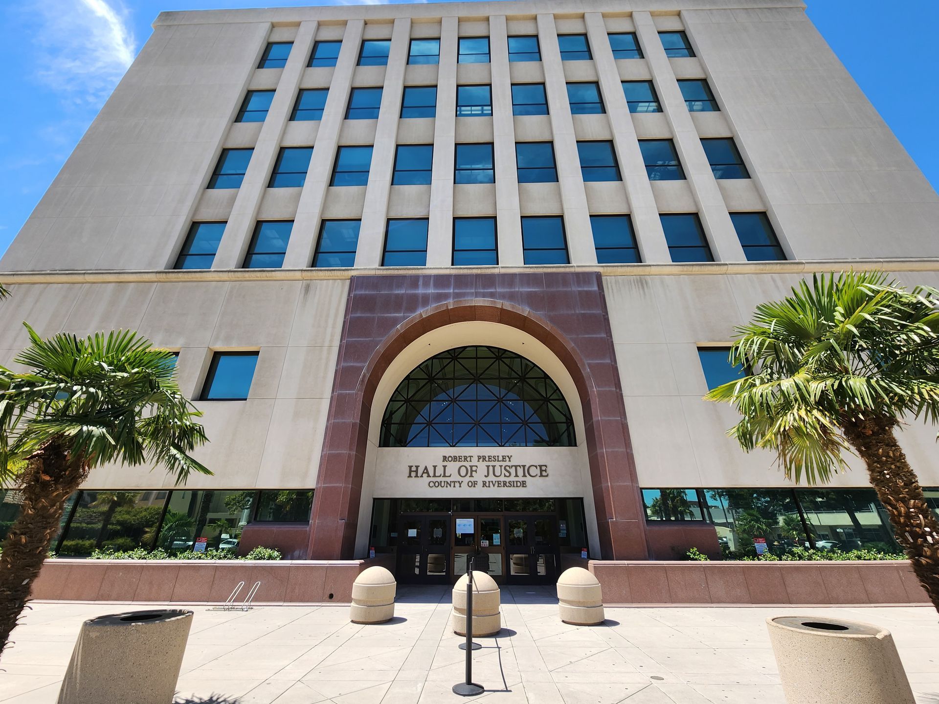 The San Joaquin County Hall of Justice building with an arched entrance, palm trees in the foreground, and blue sky.