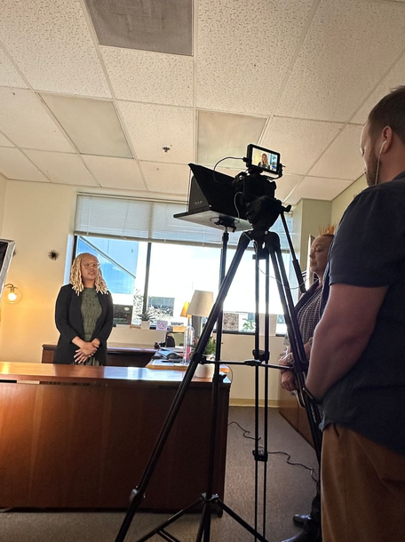 Camera crew filming a woman behind a front desk in an office lobby.
