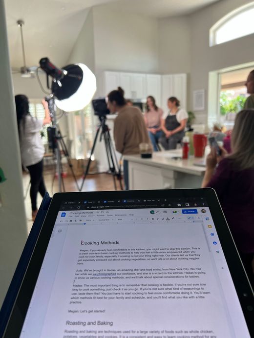 Laptop screen in foreground during a video shoot with crew and lighting setup in a bright room