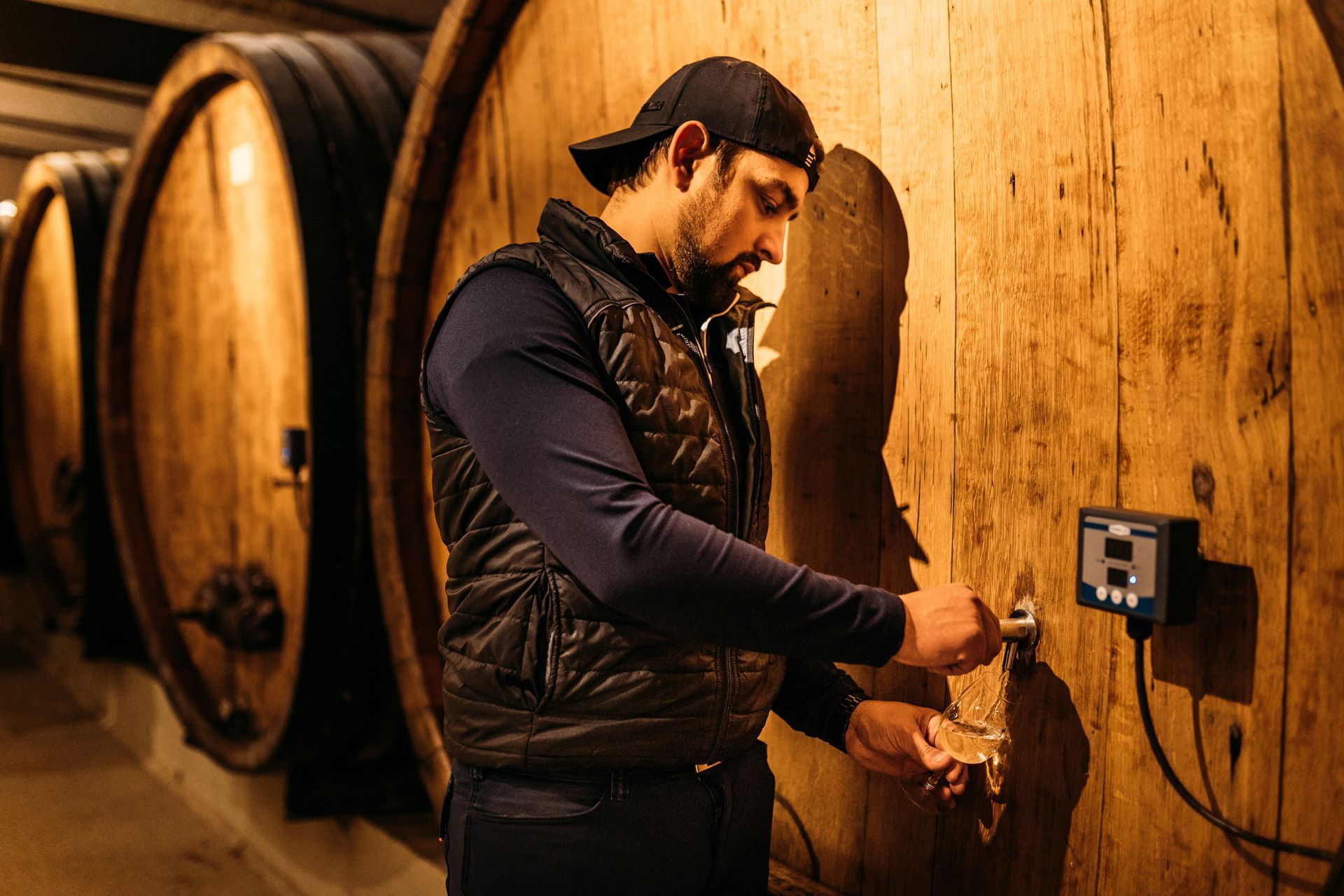 Un homme se tient devant une rangée de tonneaux en bois dans une cave à vin.